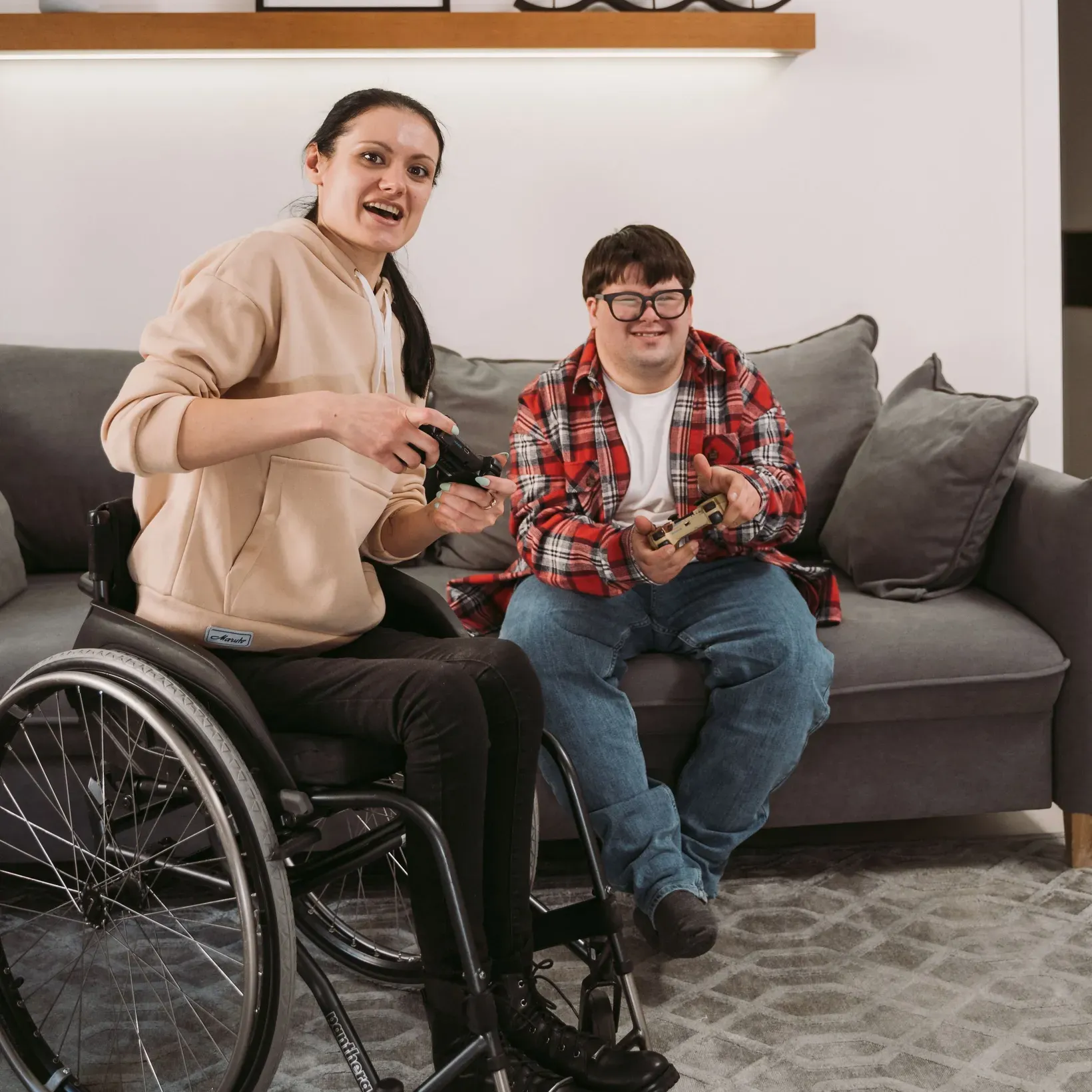 Two friends laughing over a video game at home, one seated in a wheelchair